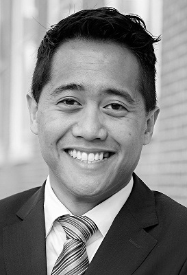 A close-up portrait of Zid Mancenid who is dressed in a suit and tie, has a short hairstyle and is smiling at the camera.