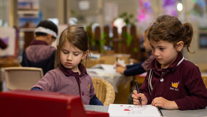 Two young children, about 4 or 5 years old, sitting at a desk with a pen and book 