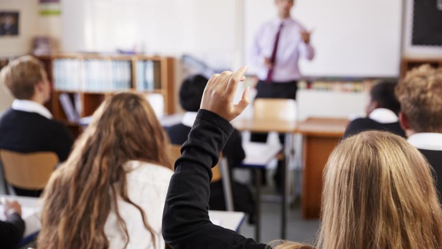 Female Student Raising Hand To Ask Question In Classroom