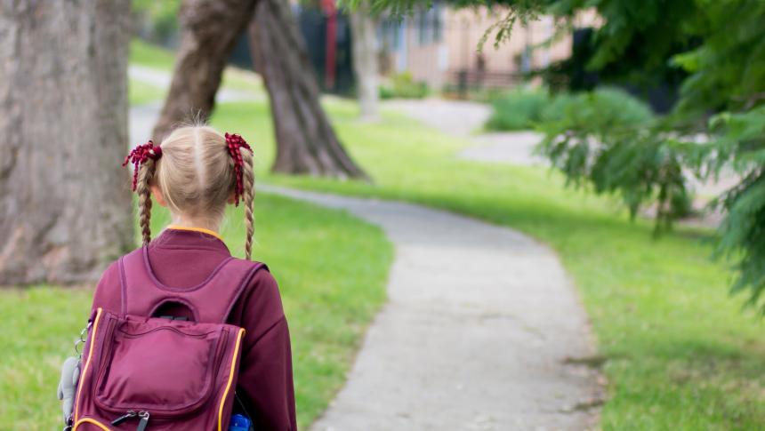 Girl in pigtails and school uniform with backpack walking home from school