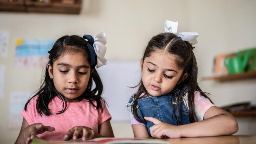 two girls reading a book at a desk