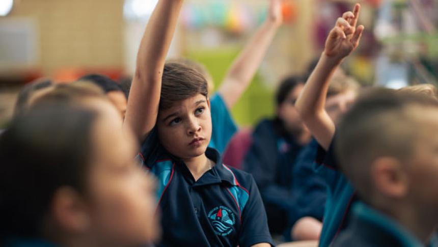 A group of children in a classroom with their hands up