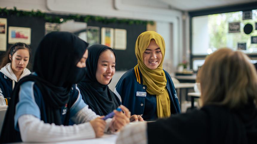A teacher sits crouched in front of three students. 
