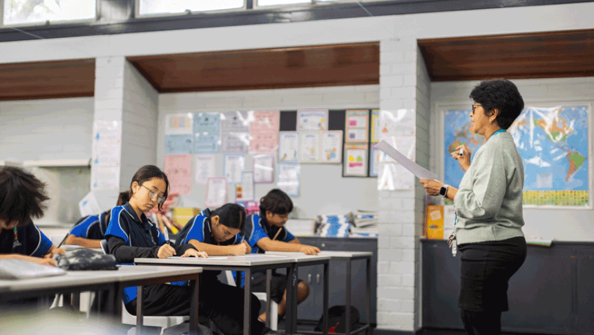 A teachers stands at the front of the class, directing students. 