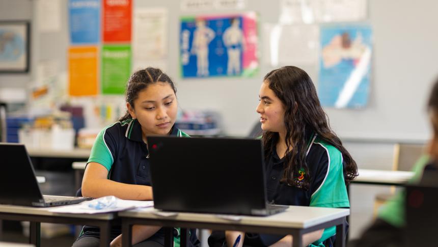 Two high school students at desk working together on laptop
