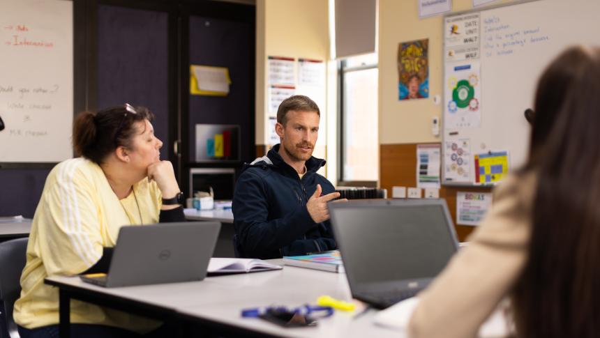Three staff members sit around a desk. One is talking while the others are listening.