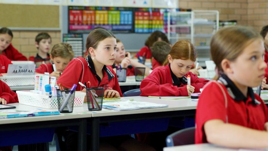 Primary school students sitting at desks listening to teacher off camera.